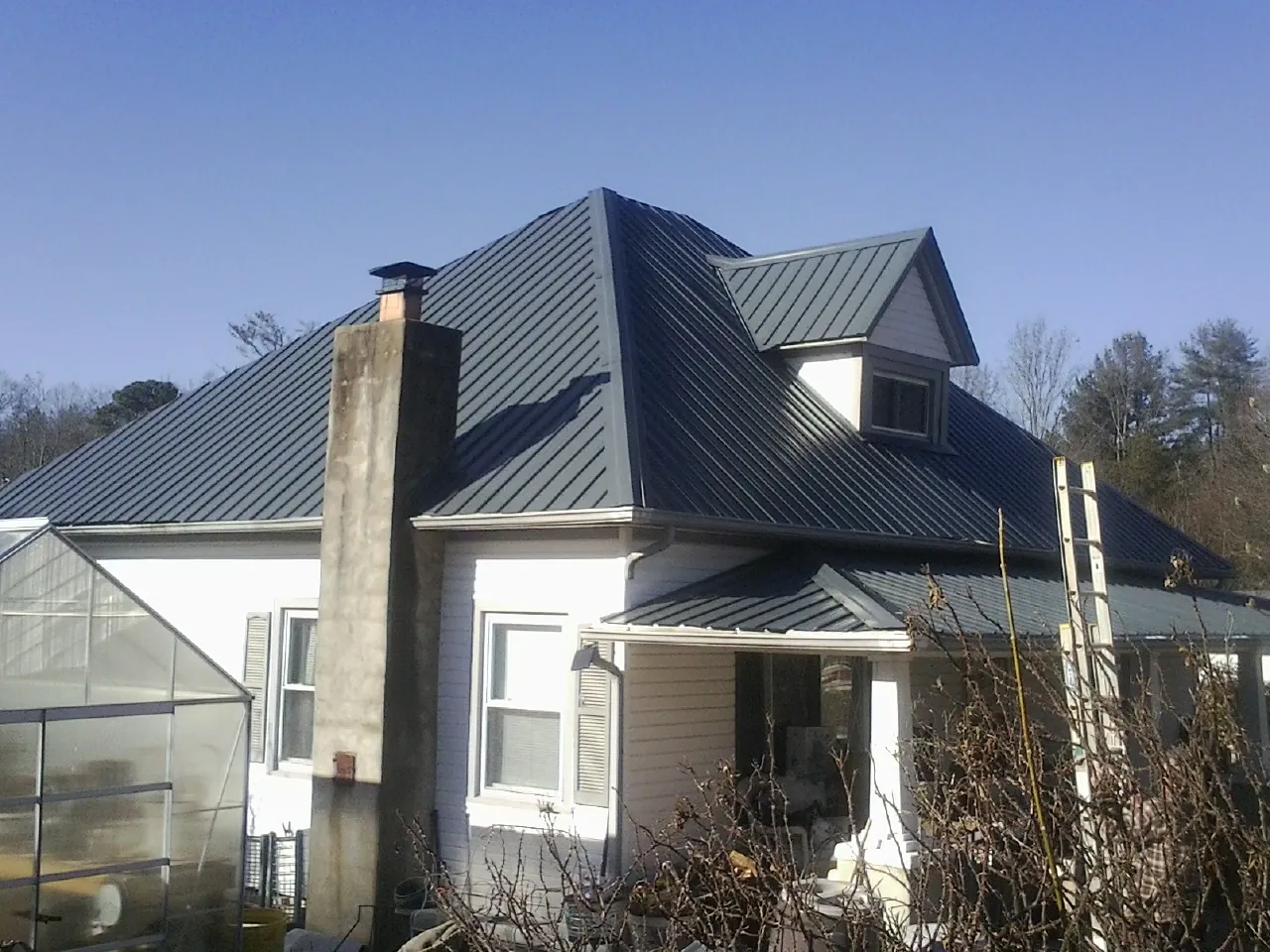 Dark blue standing seam metal roof on a white farmhouse with dormer — Slate & Tile Roof Repair by Roofing Brothers in Nanuet