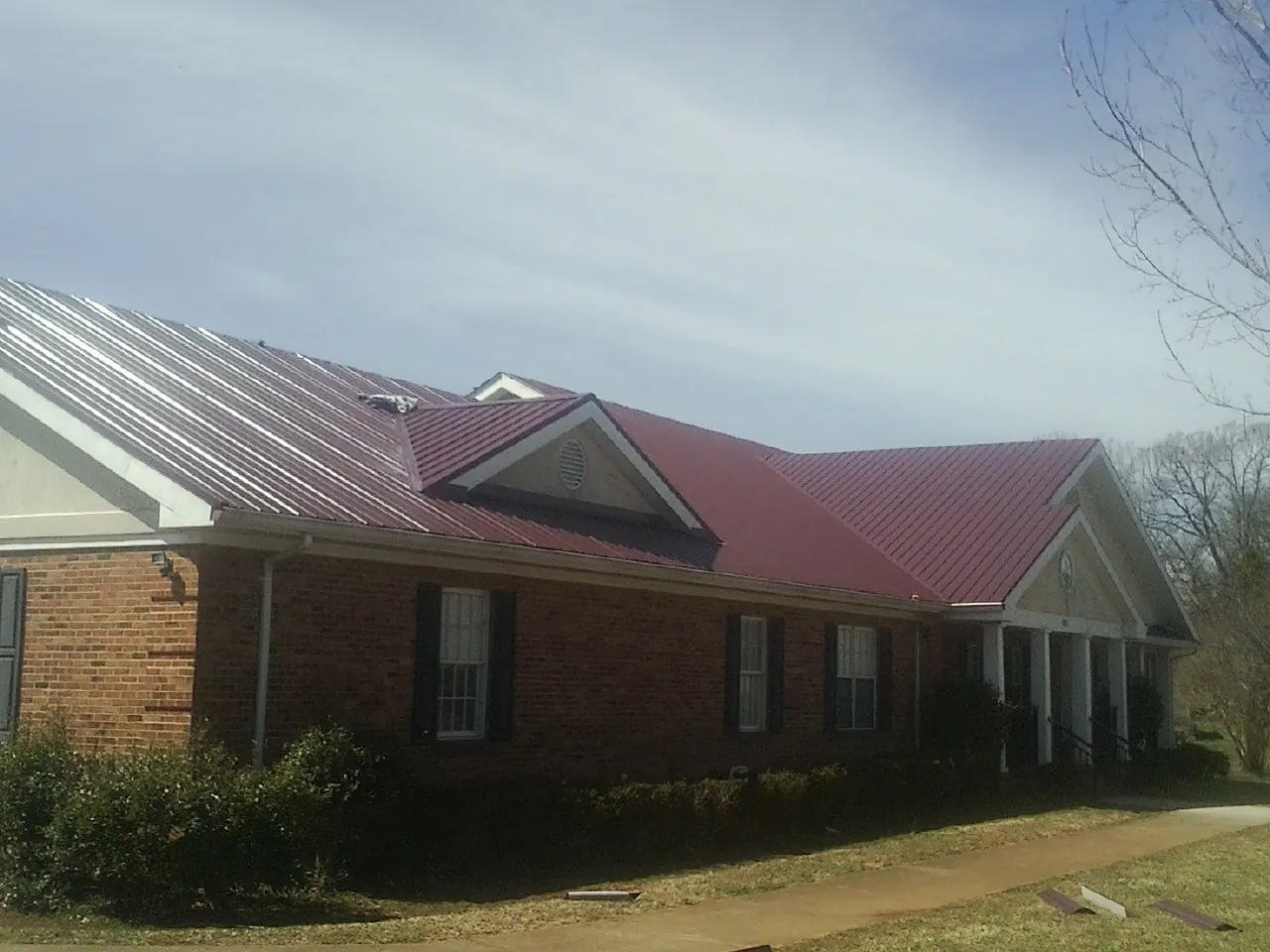 Red metal roof with gabled entries on a long brick building, from a Hail Damage Roof Repair job in Nanuet