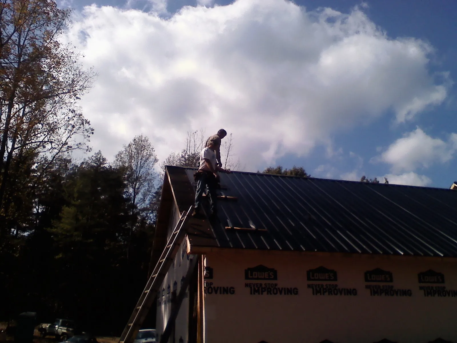Roofer fastening dark metal panels high against a cloudy sky, from a Roof Inspection job in Nanuet