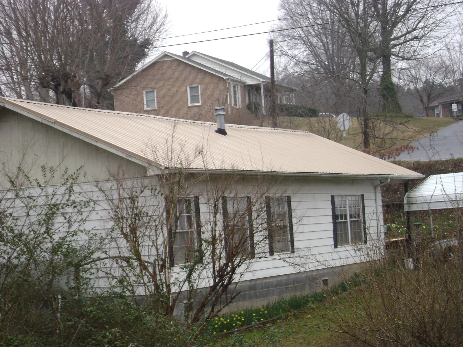 Tan metal roof on a white sided house set into a hillside — Commercial Roofing by Roofing Brothers in Nanuet
